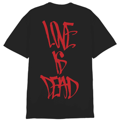 An Ink & Dagger black T-shirt showcases bold red graffiti-style text on the back that reads LOVE IS DEAD, arranged vertically down the shirt. This MAGPrinted design adds a unique edge to lettering shirts, making it a standout statement piece.